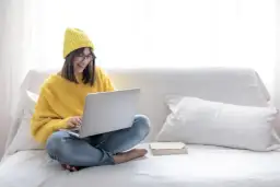 Dziewczyna w żółtym swetrze i czapce siedzi na kanapie z laptopem. Zastanawia się: "Mam domenę, co dalej?".
