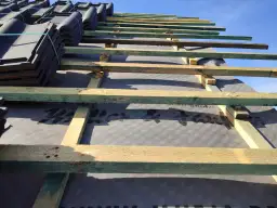 Uginajace sie panele podlogowe czekaja na montaz. Widoczna konstrukcja dachu z drewnianymi belkami i czarna membrana.