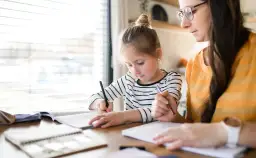 Dziewczynka z mamą uczą się w domu. Jak zacząć edukację domową? Skupienie na nauce i wsparcie rodziców.