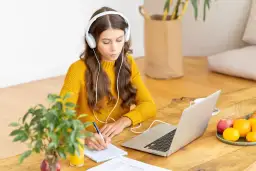 Dziewczyna w słuchawkach uczy się do egzaminów w szkole w chmurze, notując na bieżąco.