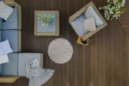 Meble rattanowe, poduszki, koc i okrągły dywanik tworzą przytulną aranżację. Idealne co na balkon na podłogę, by stworzyć relaksującą przestrzeń.
