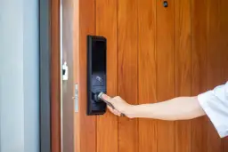 Dłoń otwiera drzwi z nowoczesnym elektrozaczepem z czujnikiem otwarcia.