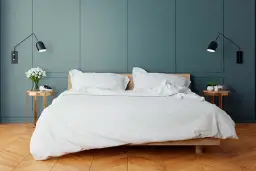 Elegancka sypialnia z białym pościelonym łóżkiem. Po obu stronach łóżka, na odpowiedniej wysokości, zamontowano czarne kinkiety, tworząc przytulną atmosferę.