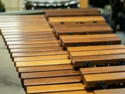 Drewniane klawisze marimby, instrumentu perkusyjnego melodycznego, obok innych instrumentów perkusyjnych niemelodycznych w tle.