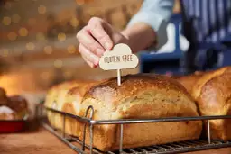 Dłoń wtyka tabliczkę "Gluten Free" w bochenek chleba. To przypomnienie, jak ważne jest, by wiedzieć, co robi gluten w organizmie, zwłaszcza przy wyborze pieczywa.