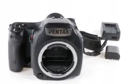 Czarna lustrzanka cyfrowa Pentax z paskiem i akcesoriami, gotowa do aukcji na Allegro.