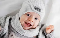 Uśmiechnięte niemowlę w szarej czapce i szaliku.
