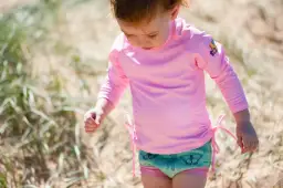 Małe dziecko w różowym stroju UV dla niemowląt z motylkami na kąpielówkach bawi się na plaży.