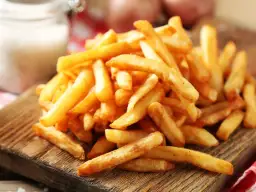 Złociste, pieczone frytki na drewnianej desce. Czy pieczone frytki są zdrowe? Z solniczką w tle, kuszą smakiem.