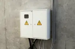 Biała skrzynka elektryczna z żółtymi symbolami ostrzegawczymi. Kto odpowiada za rury przed licznikiem? Instalacja elektryczna.