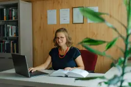 Uśmiechnięta prawniczka przy biurku z laptopem i książką. Dowiedz się, ile kosztuje sprawa o zasiedzenie u adwokata.