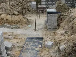 Budowa fundamentów: betonowe pustaki, zbrojenie, czarna folia izolacyjna i ziemia.