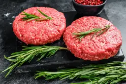 Dwa surowe kotlety na burgery z rozmarynem i pieprzem.