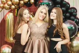 Trzy uśmiechnięte dziewczyny na 18. urodzinach, otoczone złotymi i czarnymi balonami. Zastanawiasz się, ile kosztuje fotograf na 18.?
