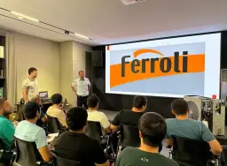 Szkolenie z serwisu Ferroli. Grupa osób słucha prezentacji na tle logo Ferroli. Kontakt do serwisu jest kluczowy.