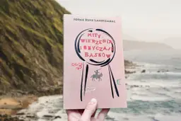 Książka "Mity, wierzenia i obyczaje Basków" Jorge Ruiza Lardizabala, z ilustracjami przedstawiającymi rycerza na koniu i inne symbole, na tle malowniczego wybrzeża.