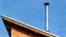 Błyszczące, zewnętrzne kominy do pieców co na tle błękitnego nieba, zamontowane na drewnianym dachu.