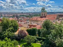 Widok na dachy Pragi z zielonym ogrodem. W oddali widać kopułę kościoła. Idealne miejsce, by zobaczyć w Pradze piękno architektury.