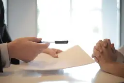 Dłonie trzymające dokument i długopis na tle jasnego okna.