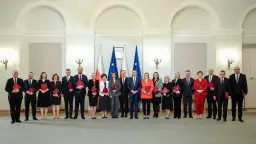 Grupa osób w eleganckich strojach, z flagami Polski w tle. Czy wśród nich jest premier Polski?