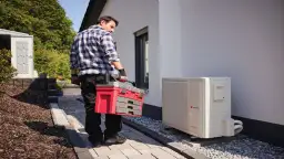 Technik z walizką narzędziową przy pompie ciepła. Regularny przegląd pompy ciepła zapewnia jej sprawność.