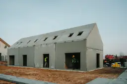 Budowa domu z gotowych elementów betonowych. Widać pracowników w kamizelkach odblaskowych.