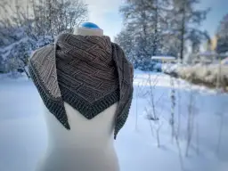 Ciepły, dzianinowy szalik po niemiecku, w odcieniach szarości, prezentowany na manekinie na tle zimowego ogrodu.