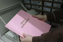 Różowa okładka pracy dyplomowej z napisem "PRACA DYPLOMOWA" w złoconych literach. W tle stosy pudeł, które mogą zawierać materiały do prezentacji.