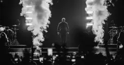 Pitbull na scenie, otoczony dymem i światłami, podczas koncertu.