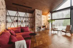 Przytulny salon w stylu wiejskim z ceglanym kominkiem, czerwoną kanapą i drewnianą podłogą.