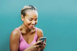 Uśmiechnięta dziewczyna z warkoczami przegląda telefon, szukając inspiracji, jak zrobić ankietę na Facebooku.