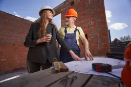 Architektka i budowlaniec omawiają plany. Dyskutują, ile trwa pozwolenie na budowę, podczas gdy budowa trwa.