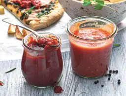 Dwa słoiki domowego sosu pomidorowego, idealnego do pizzy. Jeden z nich z łyżką pełną gęstego sosu.