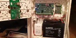 Wnętrze centrali alarmowej: płytki drukowane, transformator i akumulator. Schemat okablowania pokazuje, jak podłączyć alarm w domu.