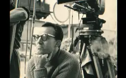 Reżyser "Zezowatego szczęścia" w okularach, zamyślony, na planie filmowym obok kamery.