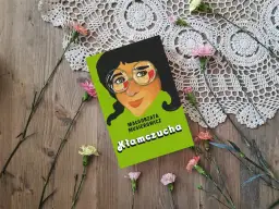 Recenzja książki "Kłamczucha" Małgorzaty Musierowicz. Okładka książki z rysunkiem dziewczynki w okularach, otoczona kwiatami na drewnianym tle.