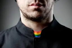 Broda i usta mężczyzny w czarnej koszuli. Widoczny tęczowy kołnierzyk, symbolizujący, co to jest pastor otwarty na wszystkich.