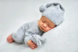 Śpiące niemowlę w szarym komplecie i czapce z uszkami, przytulające małego króliczka.