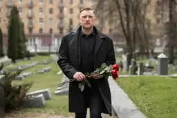 Mężczyzna w czerni, z bukietem czerwonych róż, idzie przez cmentarz. Jakby to był sen o zmarłym tacie jako żywym.