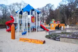 Nowoczesny plac zabaw z piaskownicą, zjeżdżalniami i domkiem dla dzieci.