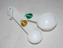 Dwie białe łyżki miarowe. Jedna ma oznaczenie 5 ml (1 TSP), druga 15 ml (1 TBS).