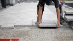 Układanie płyt tarasowych na suchym betonie. Pracownik precyzyjnie dopasowuje kolejny element, tworząc równą nawierzchnię.