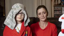 Chłopiec w czerwonym szlafroku i ręczniku na głowie wygląda jak pastuszek. Obok siedzi kobieta.