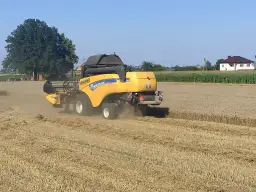 Żółta maszyna rolnicza, kombajn, pracuje na polu. Ubezpieczenie pojazdu wolnobieżnego zapewnia spokój podczas żniw.