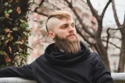 Mężczyzna z gęstą brodą i podgolonymi bokami głowy w czarnej bluzie.