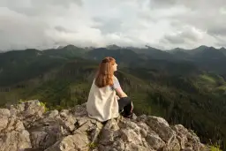 Kobieta siedzi na skale, podziwiając widok na góry. Szlak na Nosal widać w oddali.