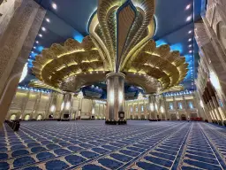 Wnętrze Wielkiego Meczetu w Kuwejcie z ozdobnym sufitem i niebieskim dywanem.