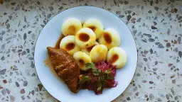 Kluski śląskie z roladą i czerwoną kapustą na talerzu.