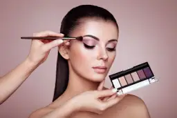 Kobieta zmysłowo maluje powieki, tworząc efekt latte makeup. W dłoni trzyma paletę cieni do powiek.