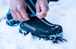 Dłonie zapinają raki na śniegu do butów wspinaczkowych.